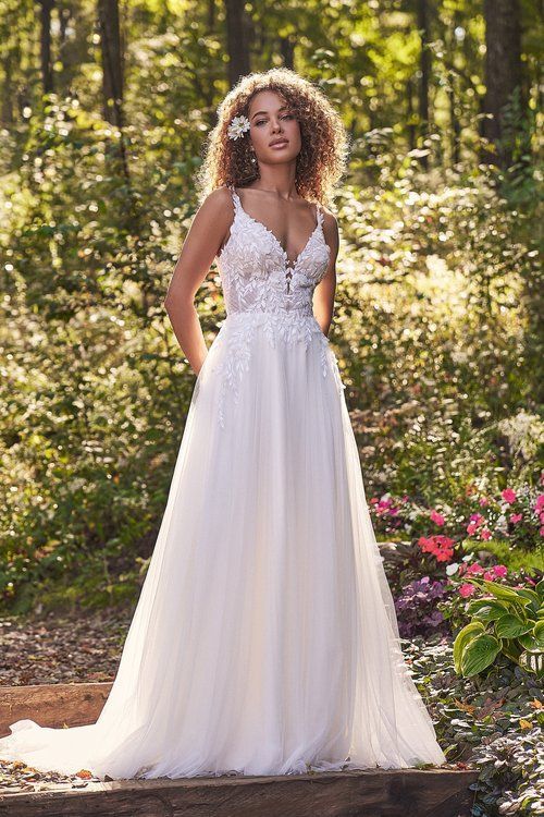 A woman in a white wedding dress is standing in the woods.