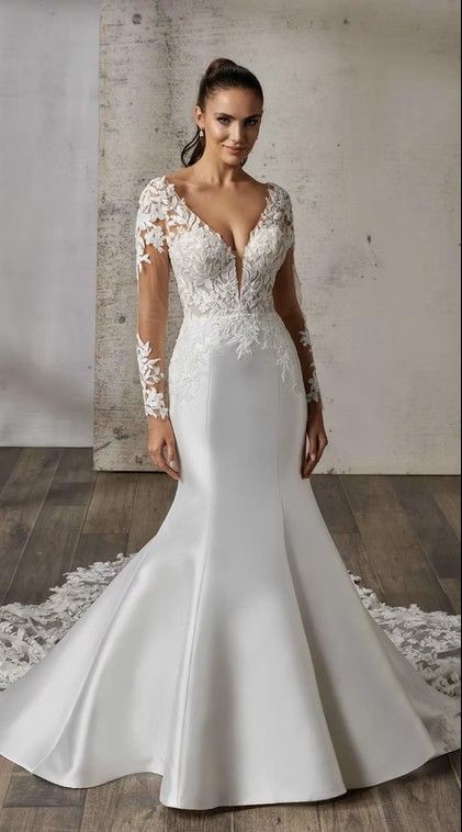 White lace wedding gown with sheer long sleeves and fitted mermaid skirt on a model against a gray backdrop. Carmela - DR2604