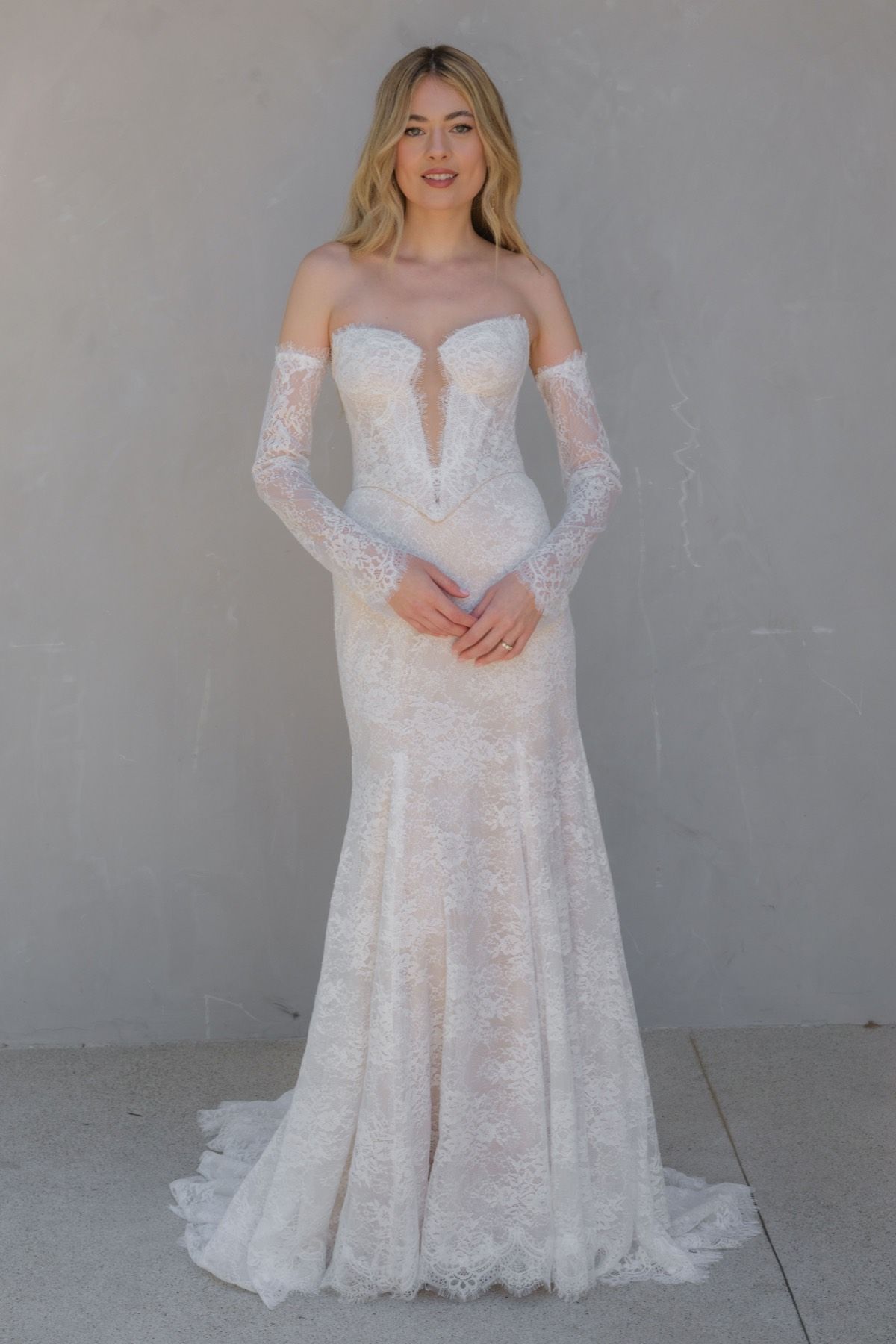 Woman in a white strapless wedding gown, standing in front of a white wall.