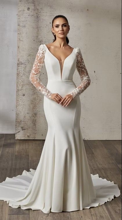 Woman in a white lace wedding gown with a long train, standing against a concrete wall. IdaliaDR2620