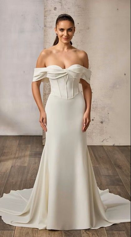 Off-shoulder white wedding gown with draped bodice and long train on a studio backdrop. Izzie -EK1866