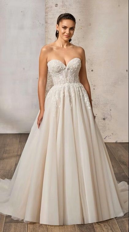 Bride in a strapless lace ball gown standing against a concrete wall. Jocelyn - EK1872