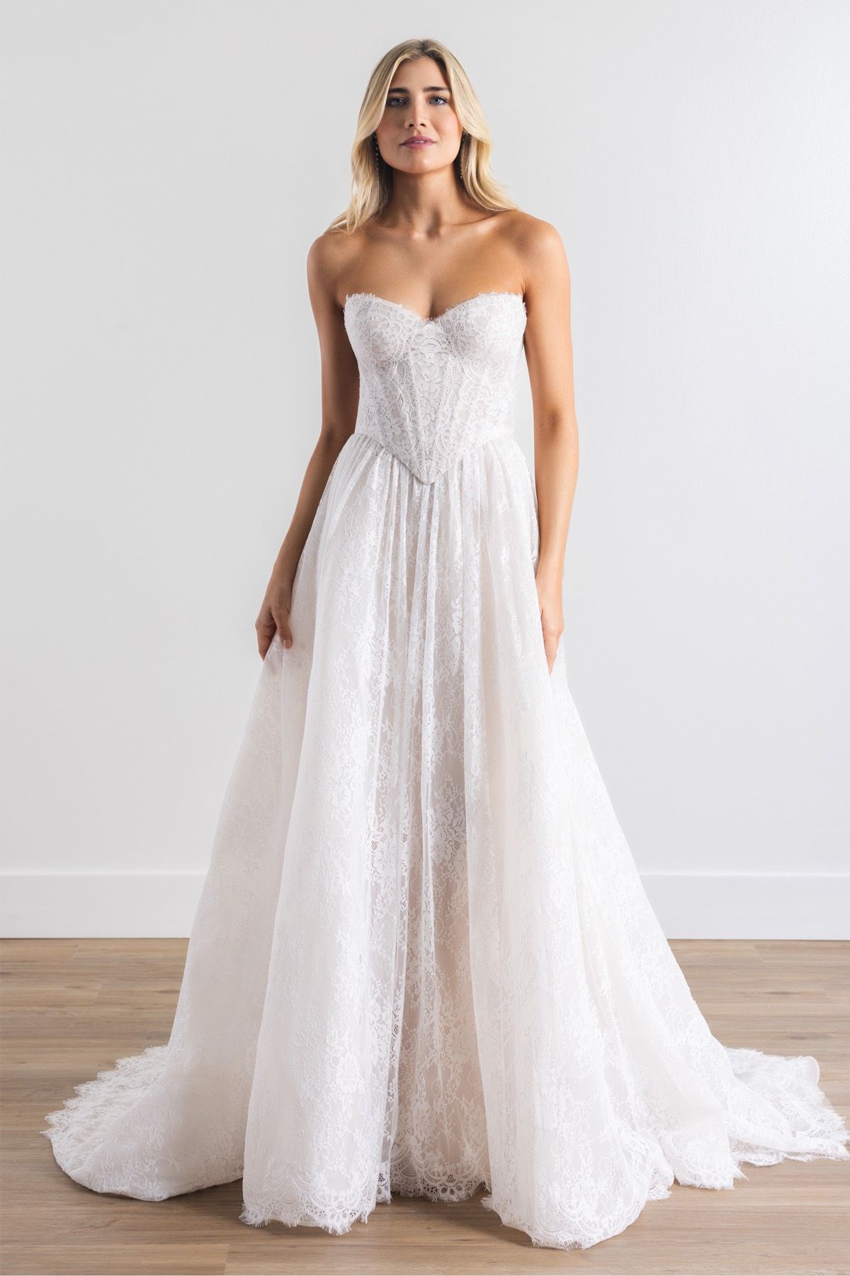 Woman in strapless white lace wedding dress, standing indoors.