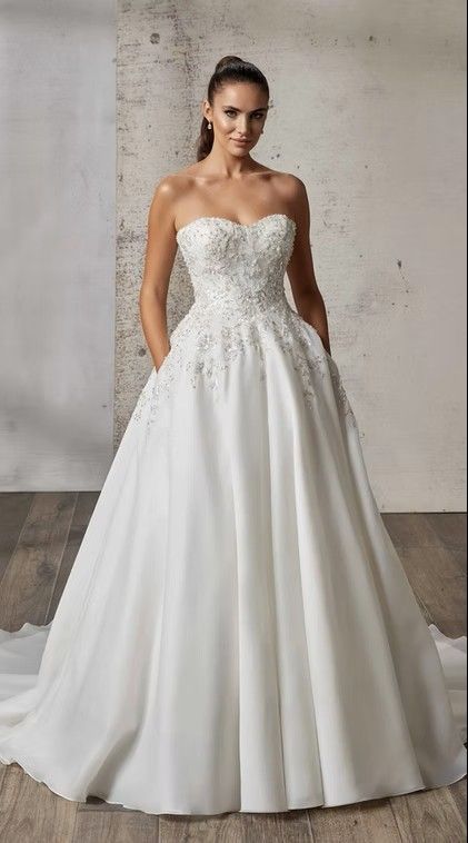 Strapless white ball gown with embroidered bodice and full skirt on a mannequin against a concrete wall. Loretta - DR2609