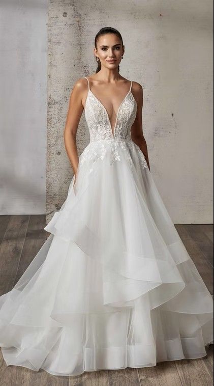 White bridal gown with deep V-neck and layered tulle skirt, modeled against a gray studio backdrop. Mafalda - DR2623