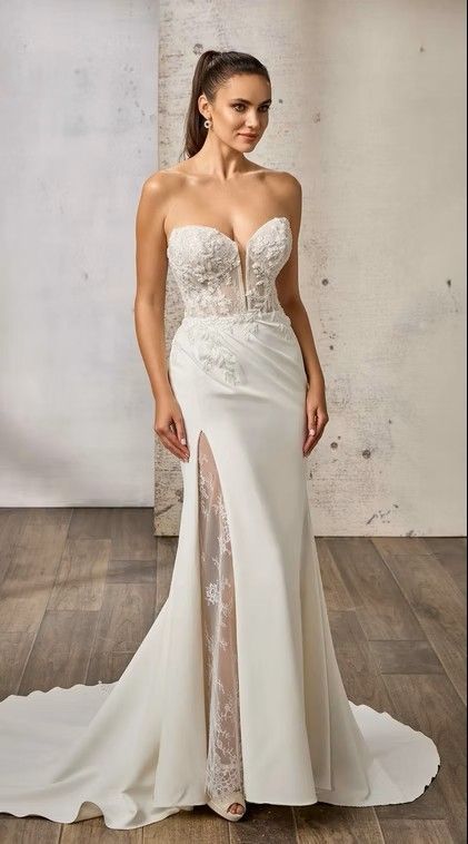 Woman in a white strapless wedding gown with lace bodice and thigh-high slit, standing on a studio floor. Maxima - DR2646