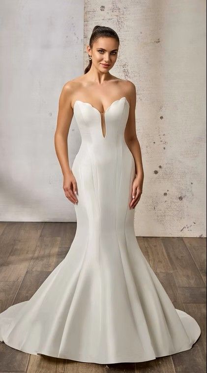 Woman in a strapless white mermaid wedding dress standing against a light wall. Prima - DR2650