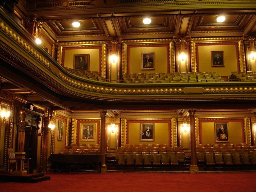 Ornate gilded theater interior with balconies, framed portraits, and warm amber lighting