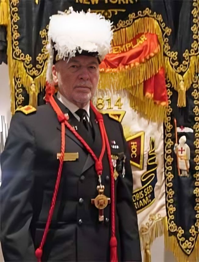 Man in formal uniform with medals and red cords stands before ornate black-and-gold Masonic banners.