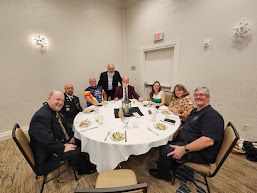 Group seated around a round banquet table in a decorated event room, smiling at the camera.