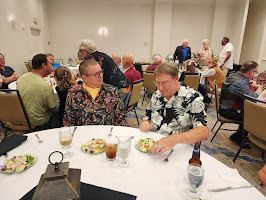 People seated at round banquet tables in a conference room, eating and talking with drinks and plates.