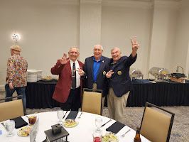 Four people posing and waving at a banquet table in a hotel event room