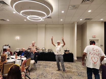 People dancing in a banquet room at a casual event, with buffet tables and circular ceiling lights.