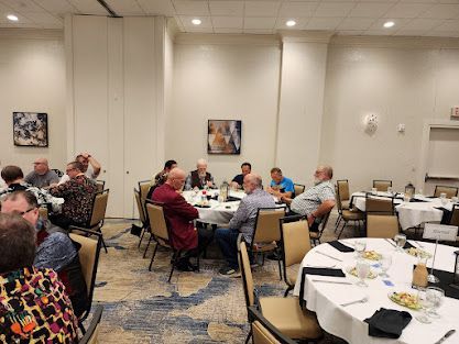 People seated at round tables in a banquet room, eating and talking during a social event.
