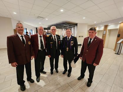 Five men in maroon blazers pose together in a bright indoor hallway.