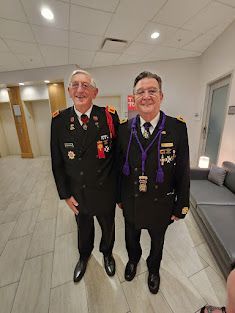 Two veterans in formal uniforms standing indoors, smiling in a hallway