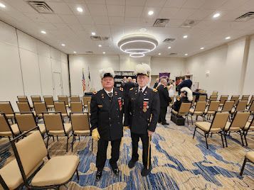 Two uniformed people standing in a conference room with rows of empty chairs and ceiling lights