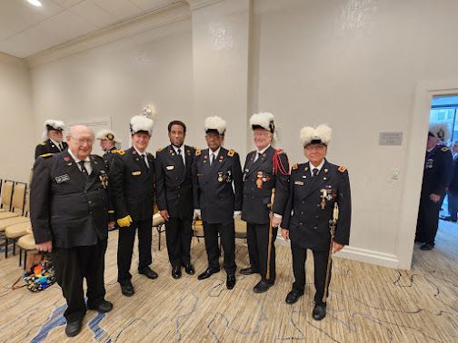 Uniformed cadets standing with an older officer in a bright indoor room at a formal event