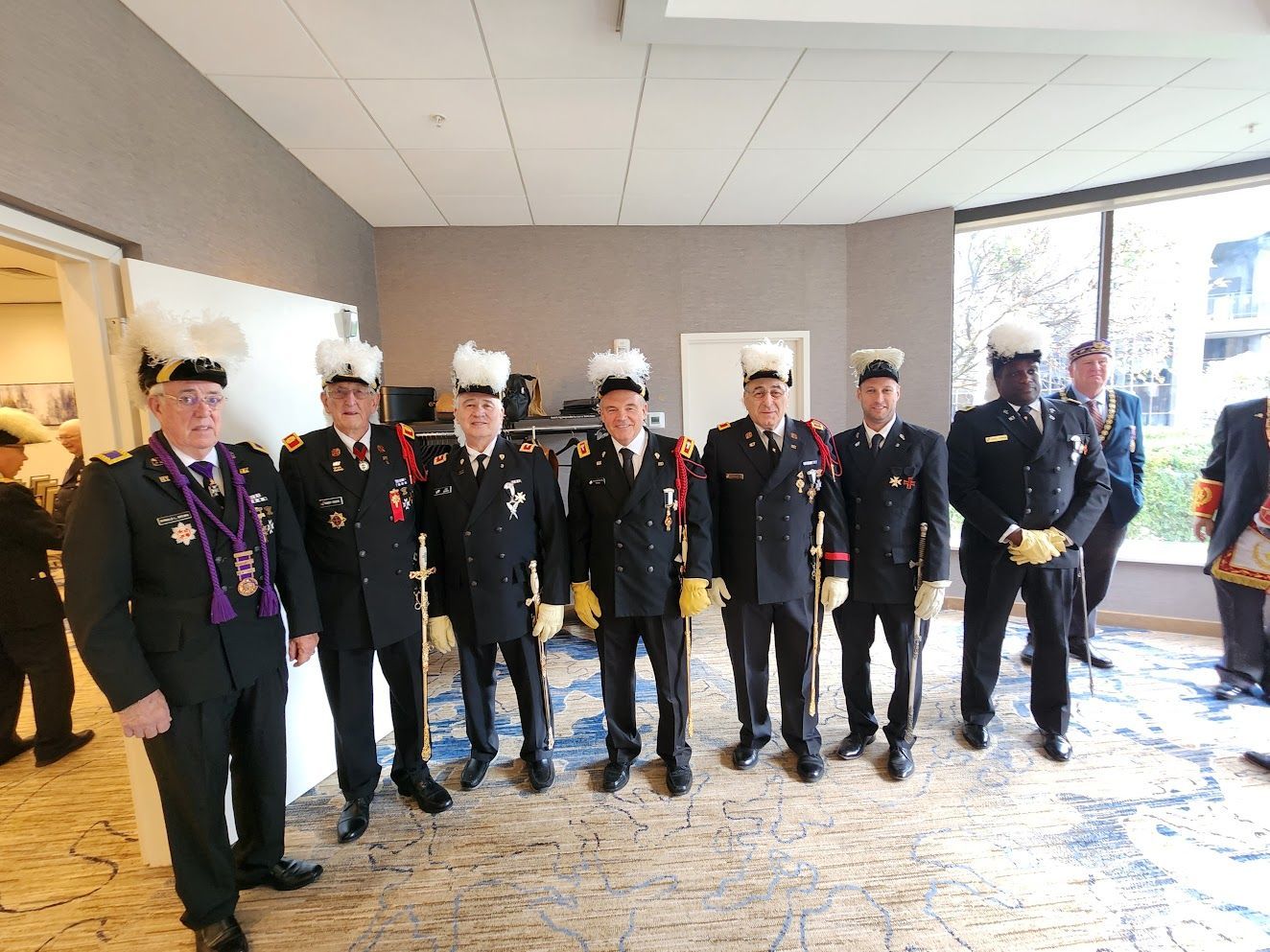 Seven uniformed veterans with white caps stand indoors, posing for a group photo.