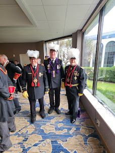 Four people in black uniforms and white hats walking in a hallway beside large windows.