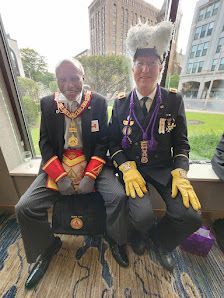 Two people in dark uniforms and gloves sit on a bench outdoors in a city park.