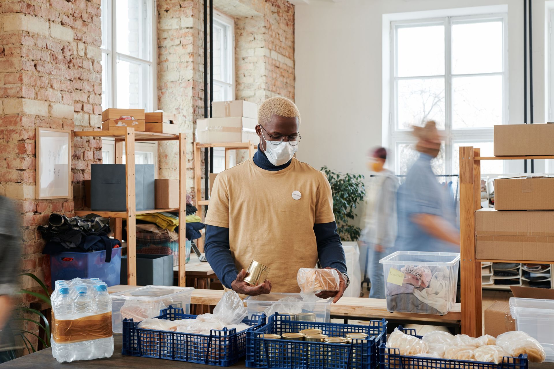 Masked volunteer packing food boxes in a bright storage room