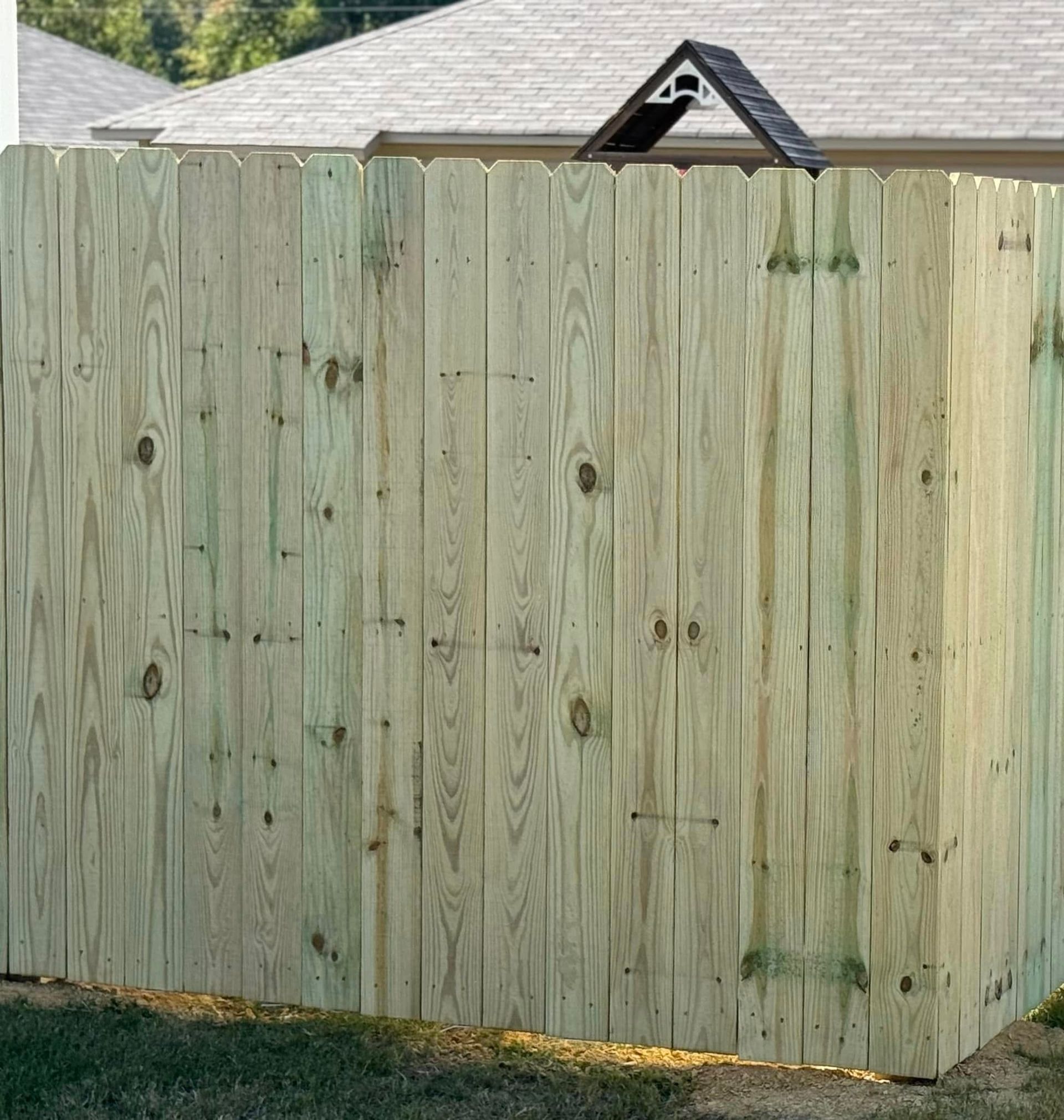 Wooden privacy fence with a house roof visible above it and a small black roof vent in the background