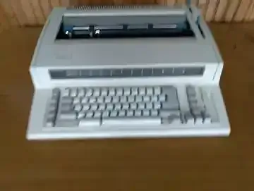 A white typewriter is sitting on top of a wooden table.
