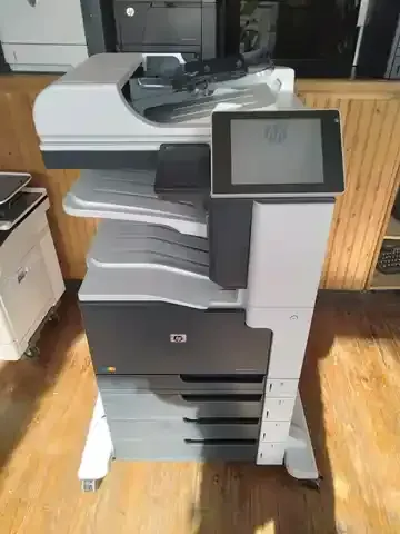 A printer is sitting on a wooden floor in a room.