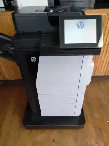 An hp printer is sitting on a wooden floor next to a wooden counter.
