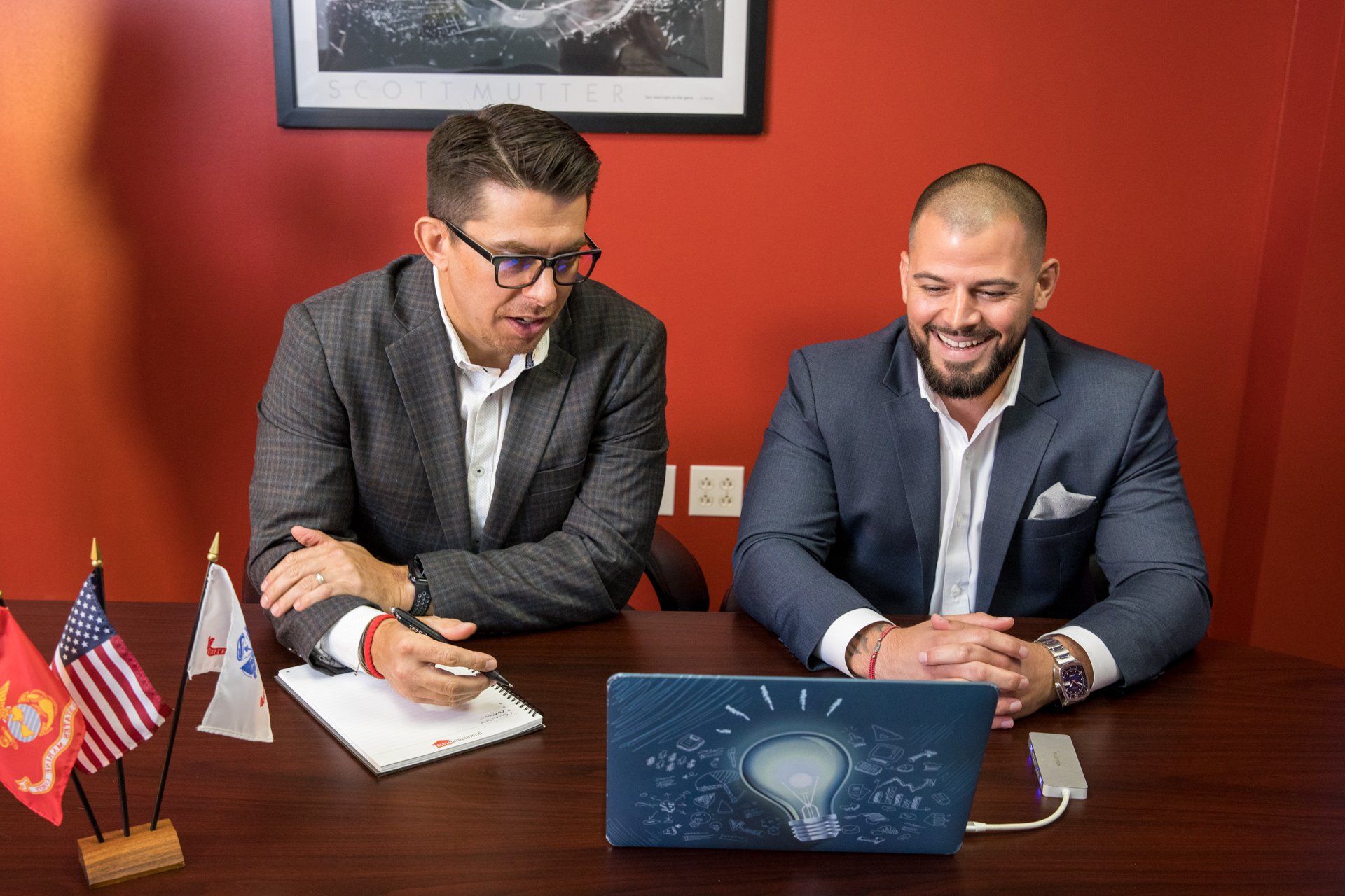 Two men are sitting at a table looking at a laptop