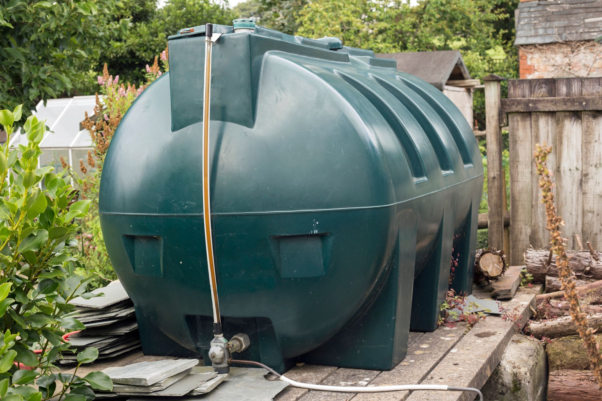 Green plastic fuel oil tank placed in a garden area with surrounding plants and grass.