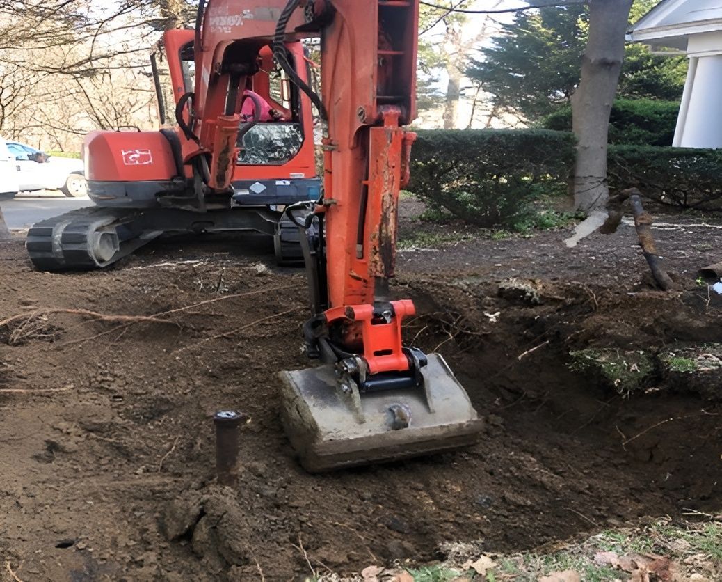 Orange excavator digging in a dirt area near a road and house.