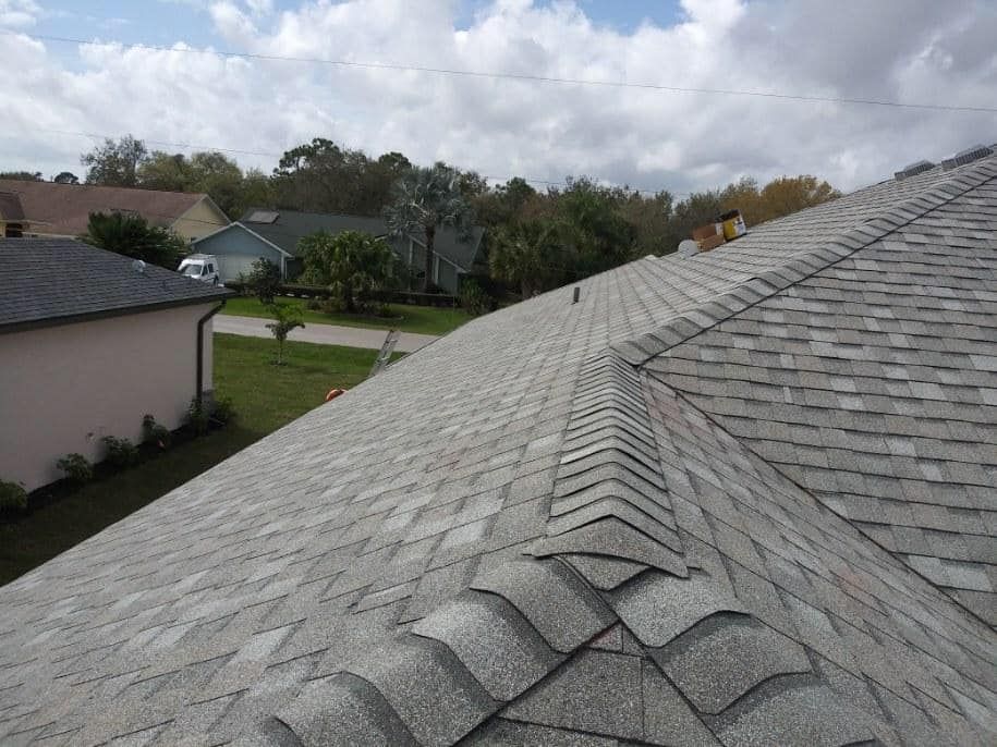 Gray shingle roof angled towards neighborhood on a cloudy day.