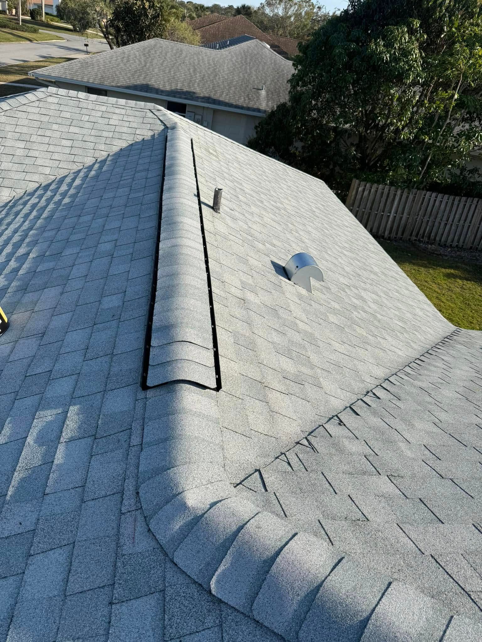 Gray asphalt shingle roof with a central vent and flashing. Sunny day, residential setting.
