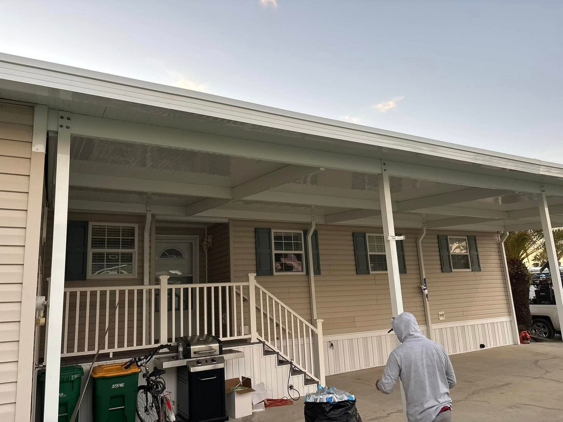 A person walks by a beige mobile home with white trim and porch.