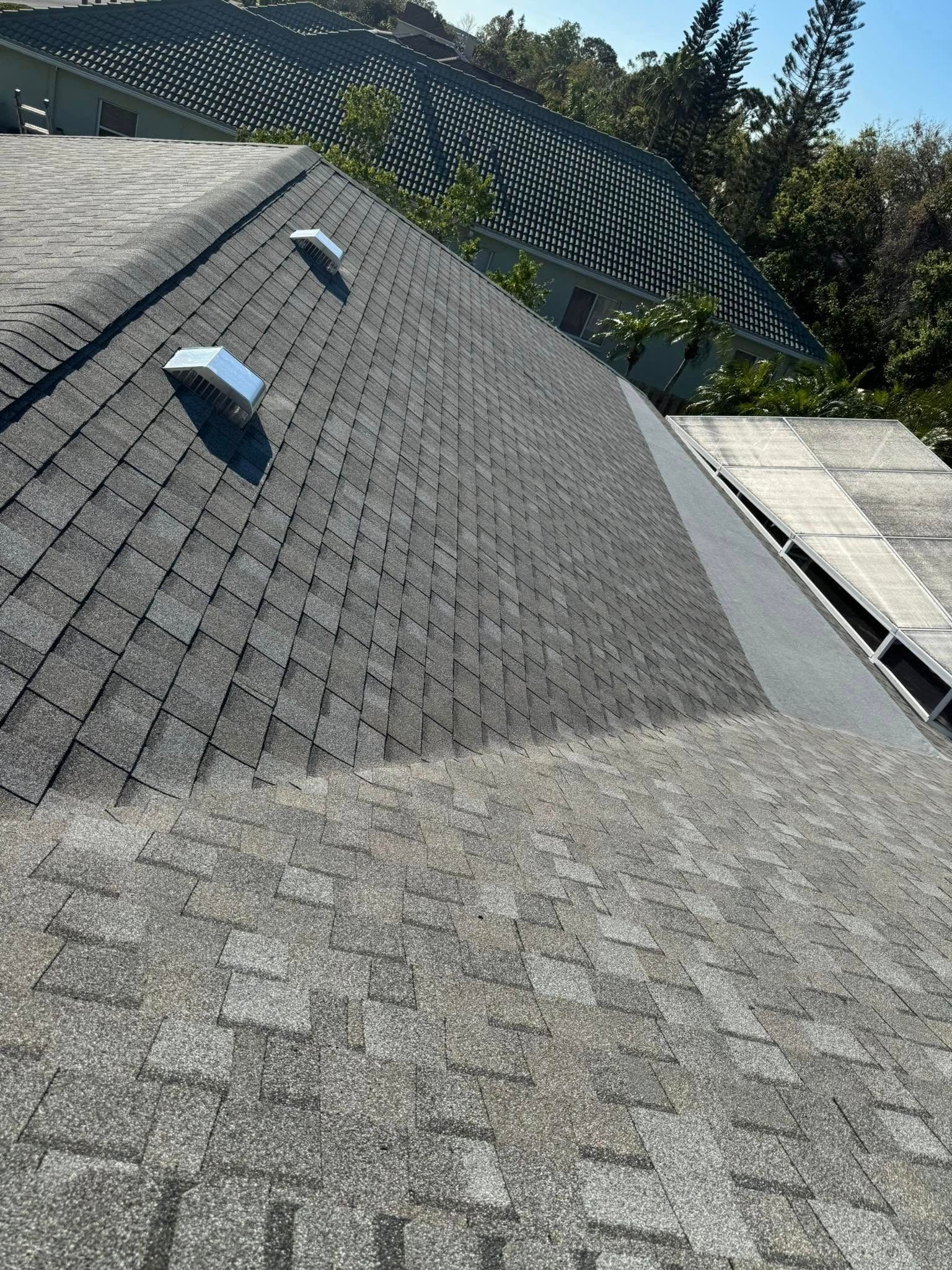 Gray asphalt shingle roof with two vents, a partially missing section, and a glimpse of a hilly background.