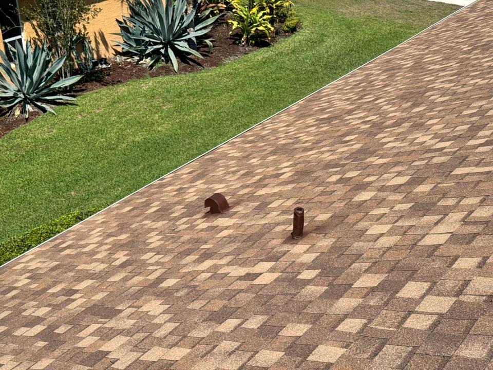 A roof with brown and tan shingles next to a grassy lawn and garden with plants.