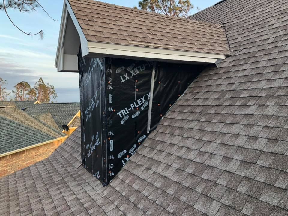 A roof with a black wrapped structure under a small, white-trimmed gable.