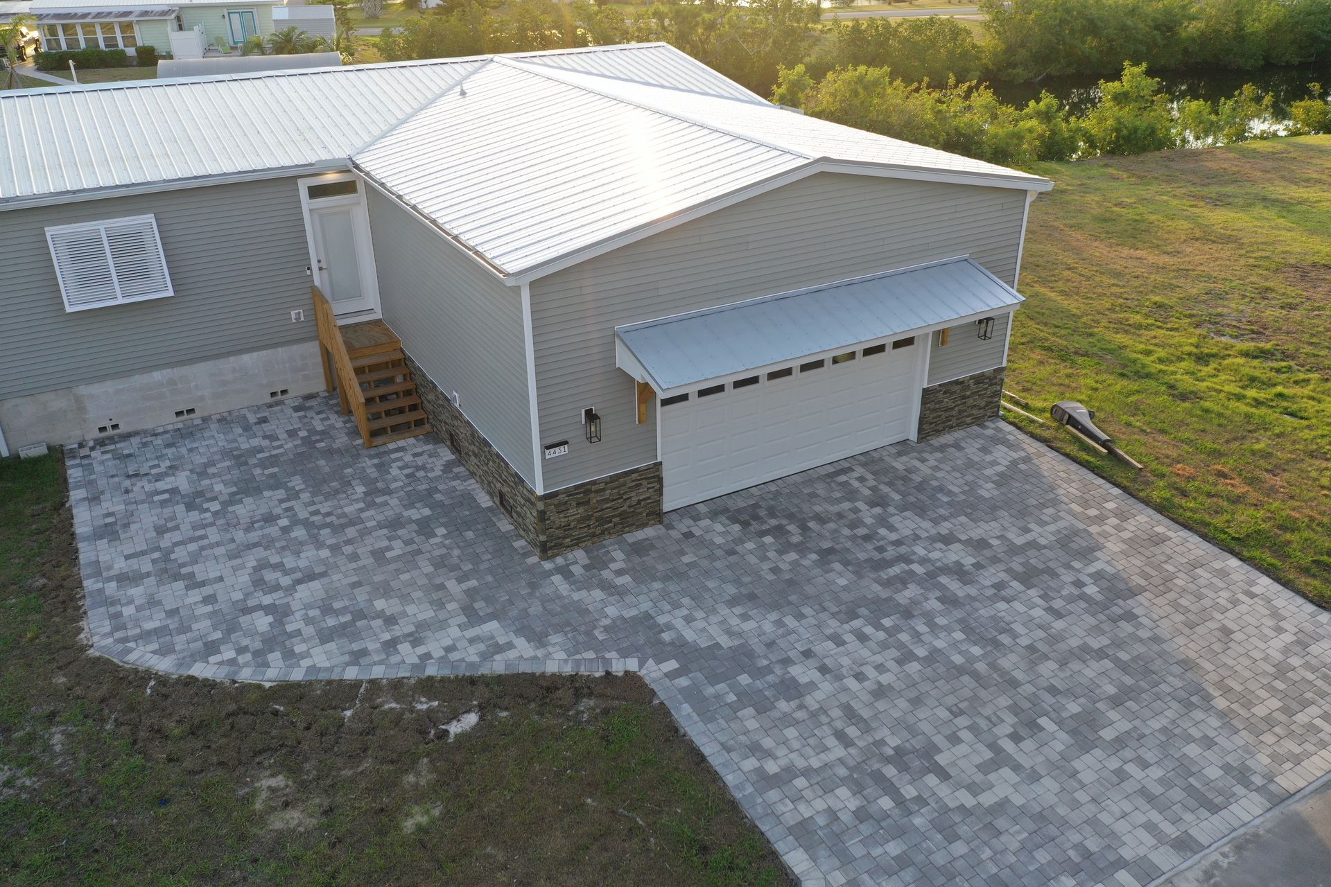 Gray house with a white garage door and brick driveway.