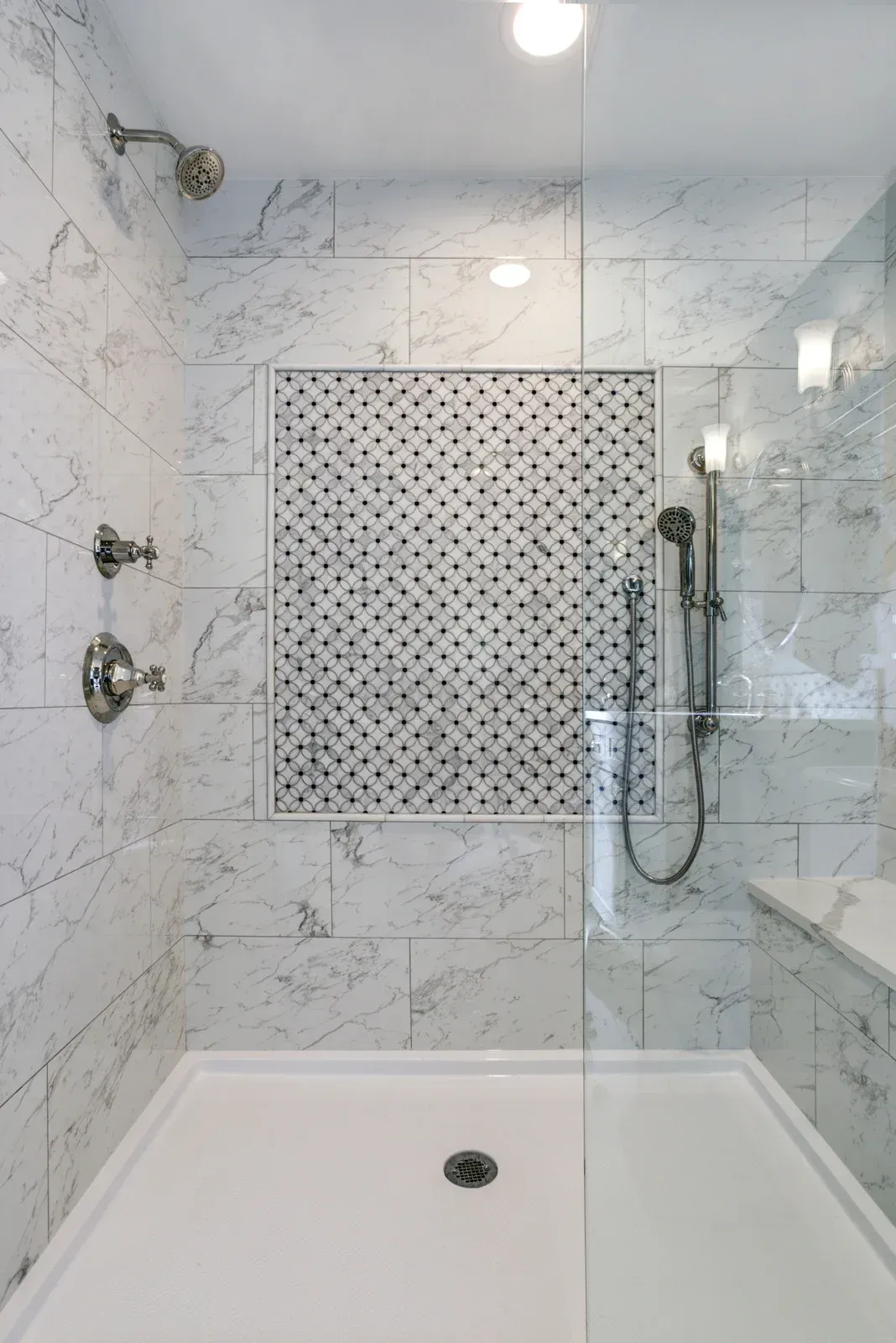 Shower with white and grey marble tile, glass door, and mosaic tile accent.