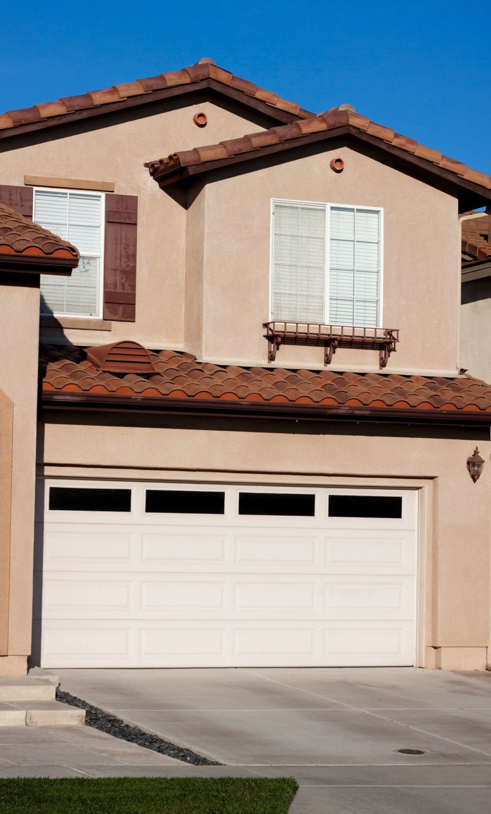 Two-story tan house with a white garage door, brown roof and accents, and blue sky.