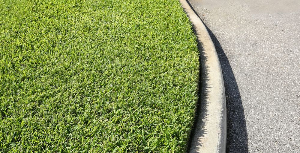 A concrete curb surrounds a lush green lawn next to a road.