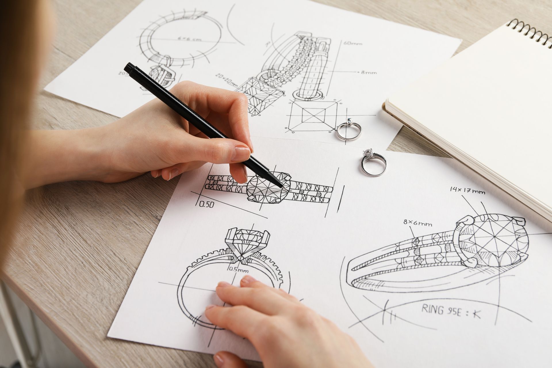 Close-up of a jeweler sketching a ring on paper at a table, showcasing a custom jewelry design.