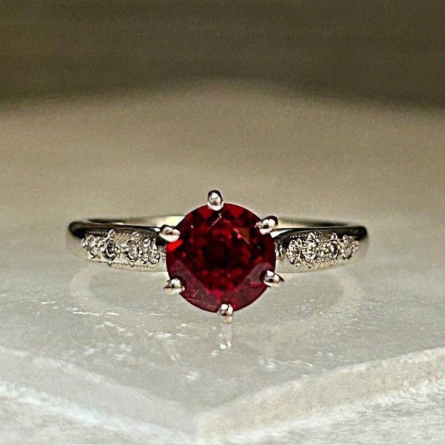 Silver ring with a round red gemstone and small clear side stones on a light background