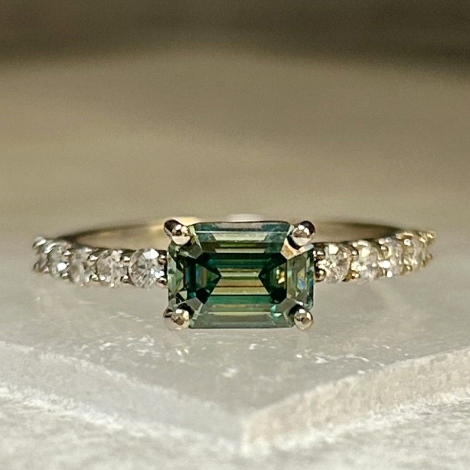 Gold ring with a rectangular green gemstone and small diamonds on the band
