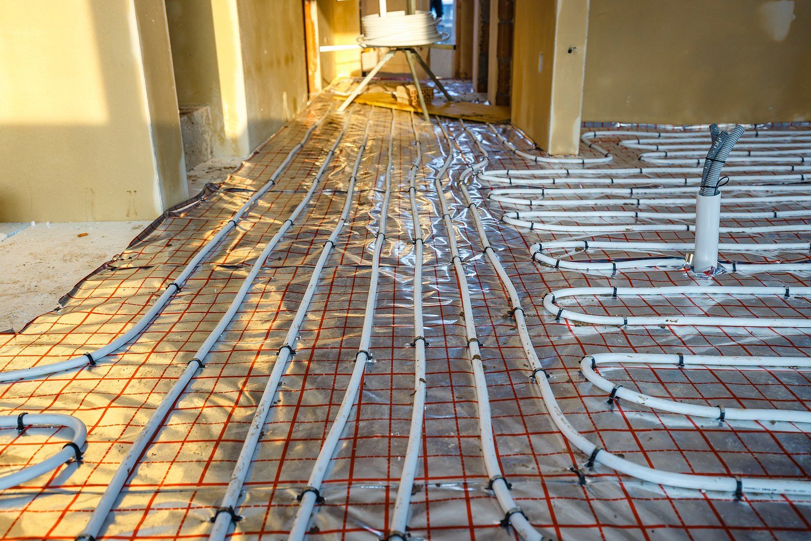 Hydronic Heating Systems in Holly Springs, NC Pipes and wiring laid across a hallway floor under construction, with walls and debris visible.