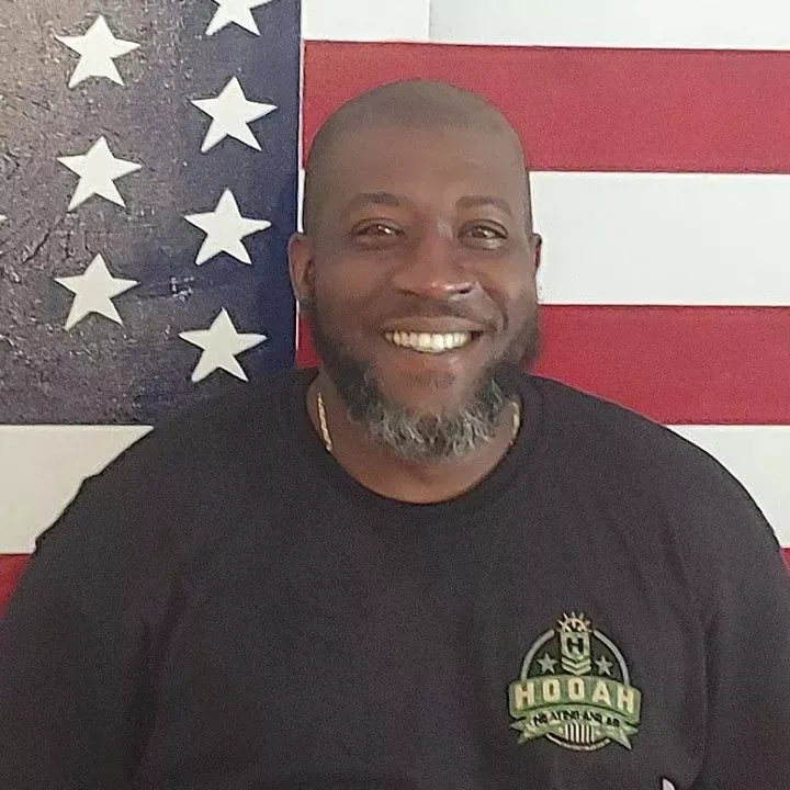 Jeffrey Cuyler Smiling man in black shirt standing before an American flag backdrop