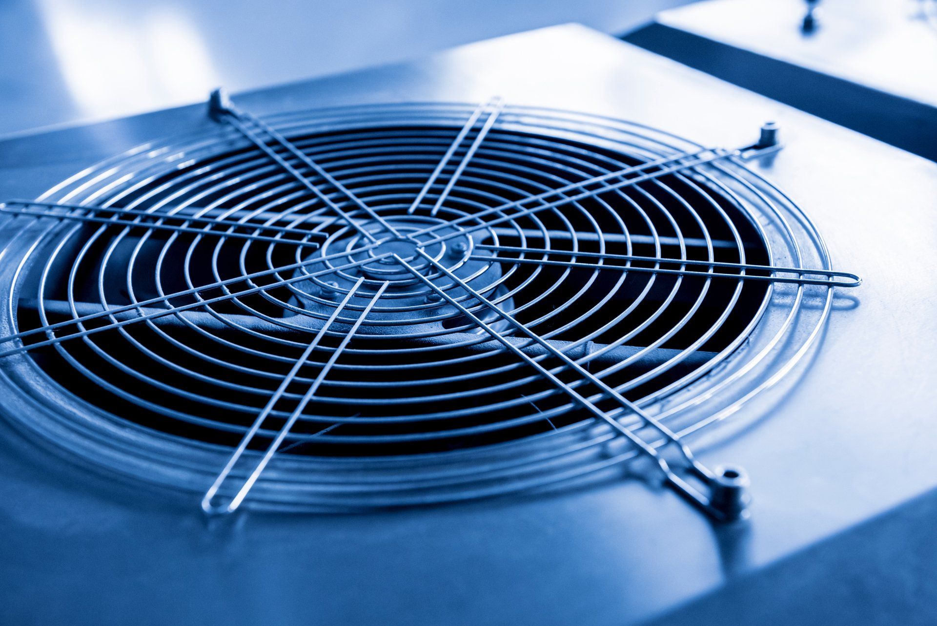 Blue-tinted close-up of a metal fan grille on an HVAC unit