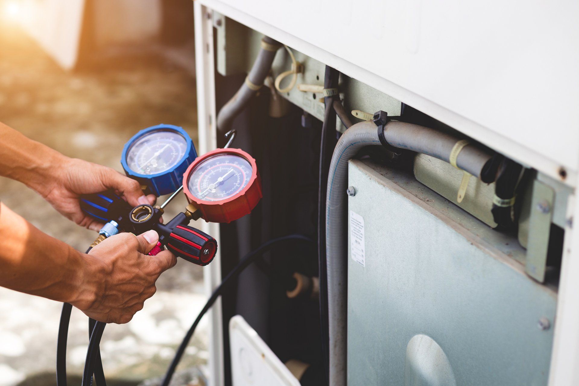 Technician using a pressure gauge to inspect HVAC equipment and refrigerant lines outdoors